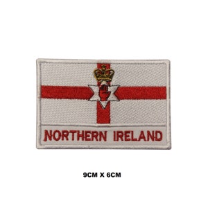 Peut inclure: Écusson brodé blanc représentant le drapeau de l'Irlande du Nord. Le drapeau présente une croix rouge sur fond blanc avec une main rouge et une couronne dorée au centre. Le texte "NORTHERN IRELAND" est brodé sous le drapeau. L'écusson mesure 9 cm sur 6 cm.