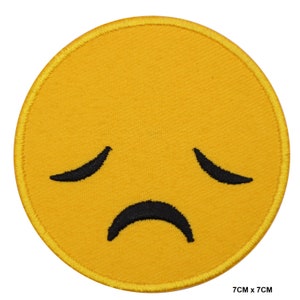 Puede incluir: Parche bordado redondo amarillo con un emoji triste. El emoji tiene cejas negras curvas y una boca hacia abajo. El parche mide 7 cm x 7 cm.