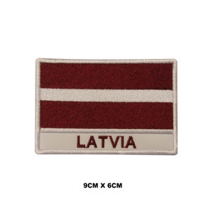 May include: Embroidered patch featuring the Latvian flag with a white stripe on a maroon background. The patch is bordered in white and has the word "LATVIA" written below the flag. The patch measures 9 cm by 6 cm.