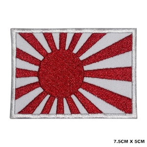 May include: A red and white embroidered patch featuring the rising sun flag of Japan. The flag has a large red circle in the center with 16 red rays extending from the circle to the edges of the patch. The patch is 7.5 inches by 5 inches.