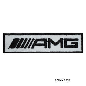 Könnte beinhalten: Ein rechteckiger Aufnäher mit den Buchstaben "AMG", schwarz auf weiß gestickt. Der Aufnäher misst 9,5 cm x 2,5 cm. Das "A" ist mit drei schrägen Linien stilisiert. Der Aufnäher hat einen schwarzen Rand.