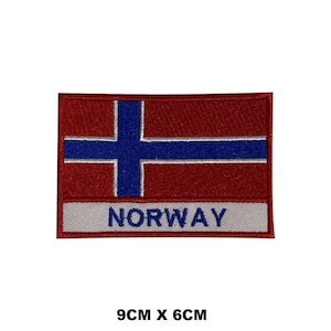 May include: An embroidered patch featuring the Norwegian flag with a red background, blue cross, and white border. The patch has the word "NORWAY" written in white on a grey background below the flag. The patch measures 9 cm by 6 cm.