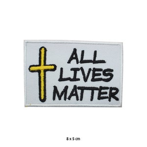 Puede incluir: Parche blanco bordado con una cruz amarilla y el texto "ALL LIVES MATTER" en letras negras. El parche mide 8 por 5 centímetros.