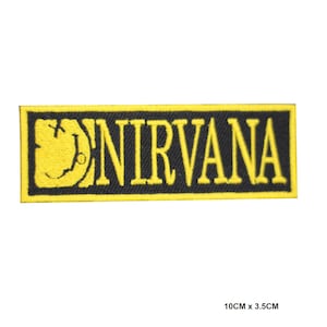 May include: A rectangular embroidered patch featuring a black background with a yellow border. The text NIRVANA is stitched in yellow capital letters next to a yellow graphic of a stylized smiley face. The patch measures 10cm x 3.5cm.