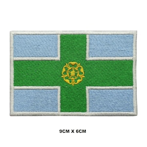 May include: An embroidered patch featuring the flag of the City of York, England. The flag is a white cross on a blue background with a green cross over the top. The green cross has a gold rose in the center. The patch is 9 cm by 6 cm.