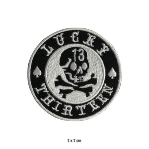 May include: Black and white embroidered patch featuring a skull and crossbones design. The skull has the number "13" on its forehead. The text "LUCKY 13 THIRTEEN" surrounds the skull and crossbones.