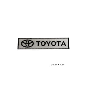 May include: A rectangular patch with the Toyota logo and name in white on a light grey background, framed by a black border. The patch measures 10.8cm x 3cm.
