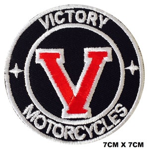Puede incluir: Un parche bordado blanco sobre fondo negro. El parche es circular y presenta el texto "Victory Motorcycles" en un círculo blanco alrededor de una "V" roja.