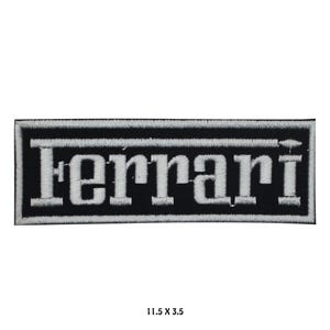 Könnte beinhalten: Ein rechteckiger, schwarz-weißer, gestickter Aufnäher mit dem Wort "Ferrari" in weißen Blockbuchstaben. Der Aufnäher misst 29,2 x 8,9 cm.