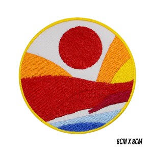 May include: Circular embroidered patch depicting a red sun over a landscape with orange, yellow, and red colours. The design includes a white sky and blue water, within a yellow border. The patch measures 8cm x 8cm.