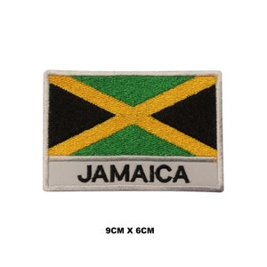Puede incluir: Parche bordado con la bandera de Jamaica en colores negro, amarillo y verde. El parche es rectangular y tiene un borde blanco con la palabra "JAMAICA" impresa en letras negras debajo de la bandera. El parche mide 9 cm por 6 cm.