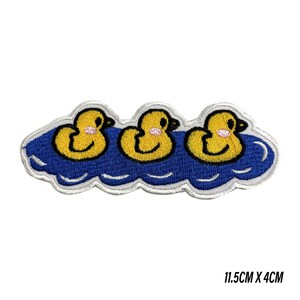 May include: Embroidered patch with three yellow cartoon ducks on blue water. The ducks have black eyes and beaks, and pink cheeks. The patch measures 11.5cm x 4cm.