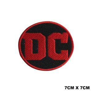 May include: A circular embroidered patch featuring the letters DC in bold red stitching against a black background, surrounded by a red border. The patch measures 7cm x 7cm, as indicated by the text printed in the corner of the image.