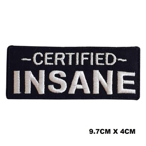 Può includere: Una toppa rettangolare nera ricamata con il testo bianco "CERTIFIED" sopra la parola "INSANE" in un carattere sans-serif in grassetto. La toppa misura 9,7 cm per 4 cm, con lettere ricamate in bianco su uno sfondo nero uniforme.