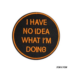 May include: A circular, black embroidered patch with an orange border. The patch displays the text "I HAVE NO IDEA WHAT I'M DOING" in orange lettering. The patch measures 7cm x 7cm.