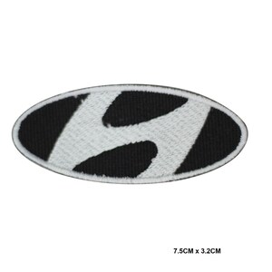 Könnte beinhalten: Ein gestickter Aufnäher mit dem Hyundai-Logo. Das Logo ist ein weißes, stilisiertes "H" auf schwarzem ovalem Hintergrund. Der Aufnäher misst 7,5 cm x 3,2 cm.