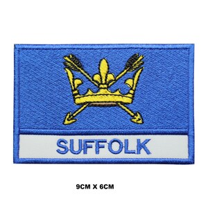 Könnte beinhalten: Blau-weißer gestickter Aufnäher mit einer goldenen Krone und Pfeilen sowie dem Wort "SUFFOLK" in weißen Buchstaben. Der Aufnäher misst 9 cm x 6 cm.