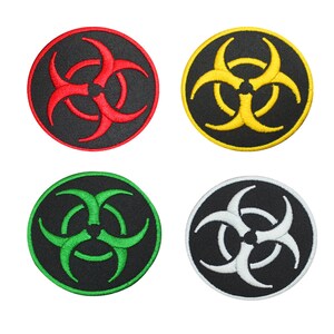 May include: Four embroidered iron-on patches featuring a biohazard symbol in different colours: red, yellow, green, and white. The symbol is a black circle with three stylised crescent shapes.