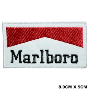 May include: A rectangular embroidered patch featuring a white background with a red chevron design at the top and the black text Marlboro centered below. The patch measures 8.9 cm by 5 cm, which is approximately 3.5 inches by 2 inches.