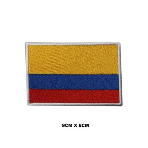 May include: An embroidered patch of the Colombian flag. The flag is yellow, blue, and red with a white border. The patch is 9 cm by 6 cm.