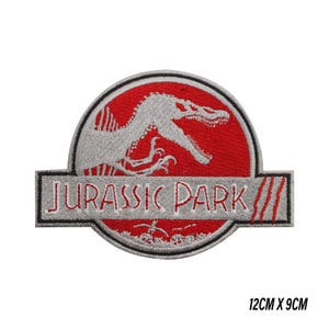 Op de afbeelding: Geborduurde patch met het Jurassic Park-logo. Het ontwerp bevat een rode cirkel met een wit dinosaurus silhouet en de woorden "JURASSIC PARK" in wit op een grijze rechthoek. Afmetingen: 12 cm x 9 cm.