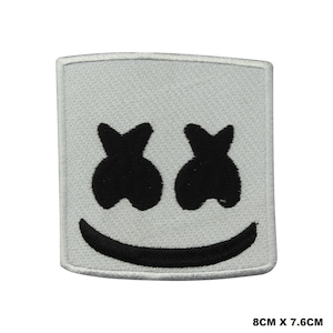 Puede incluir: Un parche bordado cuadrado con fondo blanco y un diseño cosido en negro que muestra dos ojos en forma de X y una sonrisa curva. El parche mide 8 cm por 7,6 cm, presentando detalles de bordado claros y bien definidos.