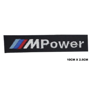 Può includere: Toppa rettangolare nera con la scritta "MPower" in bianco e un design a strisce blu, rosse e blu. La toppa misura 10 cm x 2,5 cm.