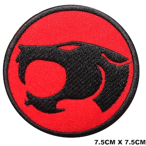 Peut inclure: Un écusson brodé circulaire présentant une silhouette de tête de chat stylisée noire centrée sur un fond rouge vif, entouré d'une épaisse bordure noire cousue. L'écusson mesure 7,5 cm sur 7,5 cm comme indiqué par le texte ci-dessous.