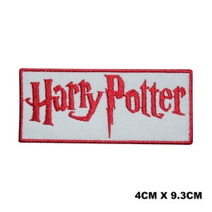 May include: A rectangular embroidered patch featuring the red text Harry Potter on a white background with a red border. The patch measures 4 cm by 9.3 cm. The lettering is in a stylised font with a distinct, jagged, and elongated design.