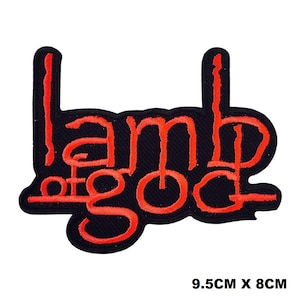 May include: A black embroidered patch featuring the red text Lamb of God in a stylised font. The patch measures 9.5 cm by 8 cm. The design consists of the words arranged in two lines with a thick black border surrounding the red lettering.