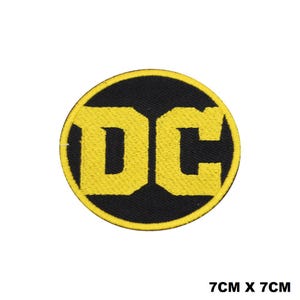May include: A circular embroidered patch featuring the letters DC in bold yellow thread against a solid black background, surrounded by a yellow border. The patch measures 7cm by 7cm as indicated by the text printed in the lower right corner.