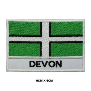 May include: White embroidered patch with a green and white flag design and the word "DEVON" in black lettering. The patch is 9 cm by 6 cm.