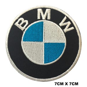 Puede incluir: Un parche bordado circular que presenta el logotipo de BMW con un anillo exterior negro, letras blancas y un diseño central de cuadrantes en azul y blanco. El parche mide 7 cm por 7 cm, según lo indicado por el texto impreso bajo el objeto.