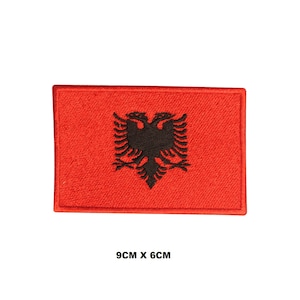 May include: Red embroidered patch with the black double-headed eagle of the Albanian flag. The patch measures 9 cm by 6 cm.