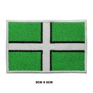 May include: Embroidered patch featuring the flag of Devon, England. The rectangular patch has a green background with a white cross, outlined in black. The patch measures 9cm x 6cm.