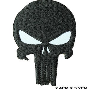 Könnte beinhalten: Ein schwarzer, bestickter Aufnäher in Form eines stilisierten Totenkopfes mit weißen Augenhöhlen und einer weißen Nasenöffnung. Der Aufnäher hat eine texturierte Garnoberfläche und misst 7,4 cm mal 5,2 cm, wie unten rechts angegeben.