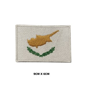May include: Embroidered patch featuring the flag of Cyprus. The rectangular patch has a white background with a gold-colored map of Cyprus, and a green olive branch. The patch measures 9cm x 6cm.