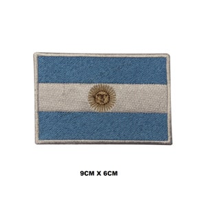 May include: An embroidered patch of the Argentinian flag. The flag is blue and white with a yellow sun in the center. The patch is 9 cm by 6 cm.