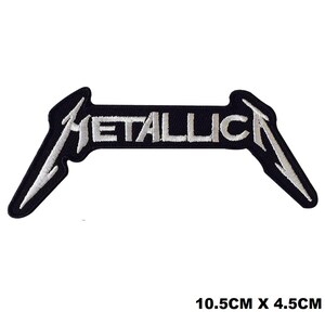 以下が含まれることがあります： 黒い背景に白い糸でMETALLICAという文字が刺繍されたワッペン。MとAの文字には、外側に伸びる細長く尖ったストロークがあります。画像に示されている通り、ワッペンのサイズは10.5cm x 4.5cmです。
