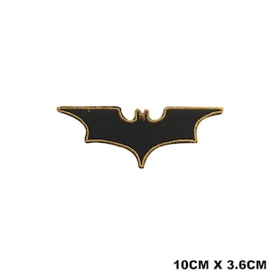 May include: Black and gold embroidered iron-on patch of the Batman logo. The logo is a stylised bat silhouette with a pointed wingspan. The patch measures 10 cm by 3.6 cm.