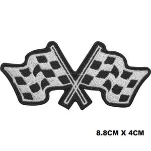 May include: Embroidered patch showing two crossed checkered racing flags in black and white. The patch measures 8.8cm x 4cm. The flags have a black border and are on white backgrounds.