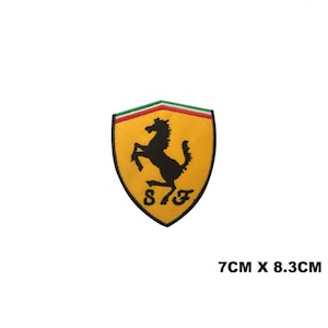 Puede incluir: Un parche bordado en forma de escudo con fondo amarillo, una silueta negra de un caballo encabritado y las letras SF en negro. El borde superior muestra franjas verde, blanca y roja. El parche mide 7 cm por 8,3 cm.