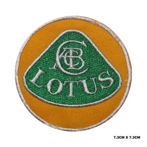May include: Embroidered patch with the Lotus logo. The patch has a yellow border and a green triangle in the centre. The word "LOTUS" is embroidered in white, along with the letters "AC" and a symbol. The patch measures 7.3cm x 7.3cm.