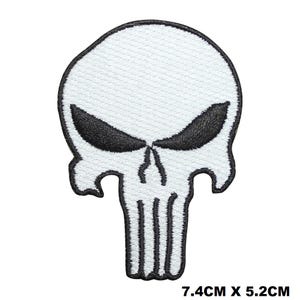 May include: An embroidered patch featuring a white skull design with black outlines and eye sockets. The patch measures 7.4 cm by 5.2 cm. The skull has a wide, jagged jawline and narrow eyes, with a distinct black border surrounding the white shape.