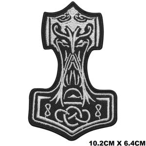 May include: An embroidered patch in the shape of a Mjolnir hammer, featuring a black background with white thread detailing a stylised knotwork design. The patch measures 10.2 cm by 6.4 cm and has a thick black border outlining the entire shape.