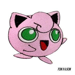 May include: Pink embroidered patch featuring a cartoon character with large green eyes, black ears, and a red mouth. The patch measures 7cm x 6.5cm.