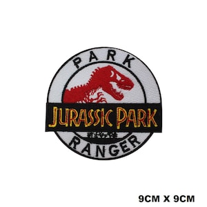 May include: A circular embroidered patch measuring 9cm x 9cm featuring a white background with a black border. It displays a red dinosaur silhouette, the text PARK at the top, RANGER at the bottom, and a black horizontal bar with JURASSIC PARK in yellow.