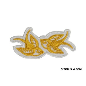 May include: Gold embroidered patch with two stylized birds facing each other. The patch is outlined in white and measures 5.7 inches by 4.5 inches.