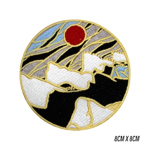 May include: Round embroidered patch depicting a mountain scene with a red sun, blue sky, and white clouds. The patch measures 8cm x 8cm. The design incorporates black, grey, and gold detailing.
