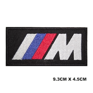 Puede incluir: Parche rectangular negro con el logotipo "M" bordado en blanco, con rayas azules y rojas. El parche mide 9,3 cm x 4,5 cm.